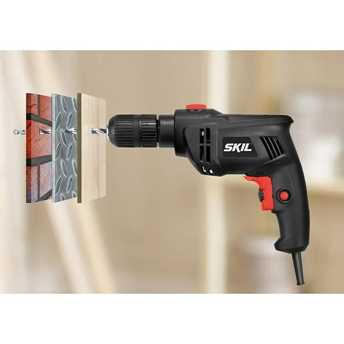 Skil Schlagbohrmaschine 1020 AA - 550 W, Schnellspannbohrfutter - Abbildung einer schwarzen SKIL Bohrmaschine beim Bohren durch verschiedene Materialien. Vielseitiges Werkzeug für Heimwerkerprojekte.