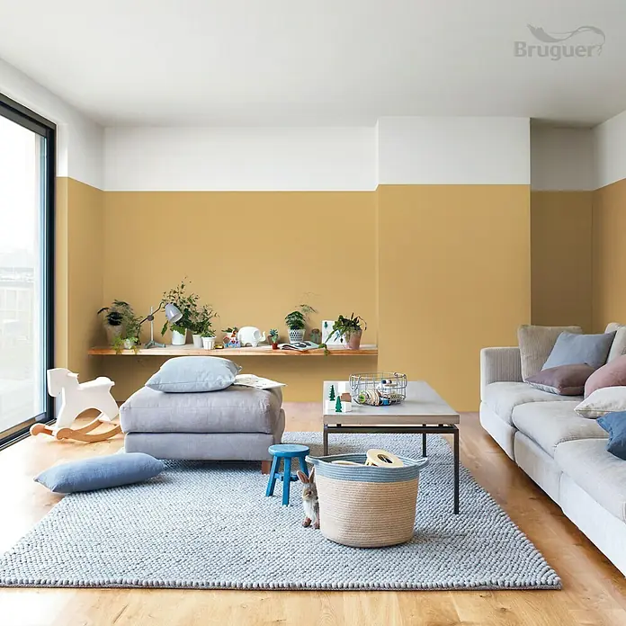 Bruguer Ultra Resist Pintura para paredes - Amarillo imperial, Mate, 4 l - Salón con sofá beige, alfombra gris, suelo de madera y paredes coloridas.