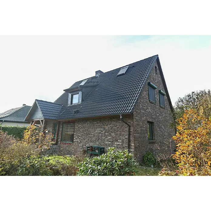 Celina Klinker Verblendstein-Ecke Montana Ravenna - 21,5 cm x 6,5 cm x 15 mm, Braun, Steinoptik - Ein zweistöckiges Backsteinhaus mit dunklem Ziegeldach und grünen Fensterrahmen, umgeben von üppigem Grün.
