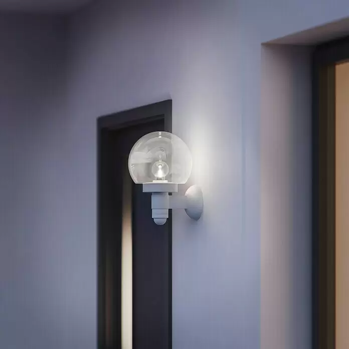 Steinel Aplique exterior con sensor L 115 S - 60 W, L x An x Al: 25,7 x 21,5 x 33 cm - Aplique de pared esférico blanco con globo transparente y sensor, montado en una pared.