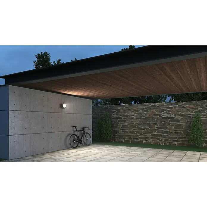 Steinel Proyector LED XLED ONE - 17,8 W, L x An x Al: 17,3 x 22,9 x 19,5 cm, Acero inoxidable, Blanco cálido - Una luz exterior moderna ilumina una bicicleta contra una pared de hormigón, mostrando una solución de iluminación elegante y segura.