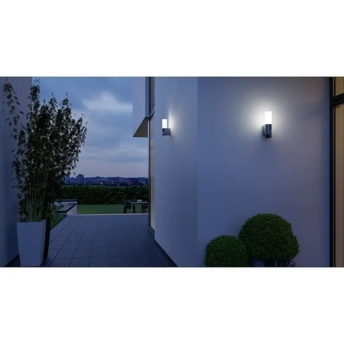 Steinel LED-Sensor-Außenwandleuchte L 605 S anthrazit - 11,3 W, L x B x H: 13,1 x 7,8 x 26 cm, Anthrazit, Warmweiß - Zwei moderne Wandleuchten außen an einer weißen Wand, die ein warmes Licht ausstrahlen. Die Leuchten akzentuieren das Gebäude stilvoll.