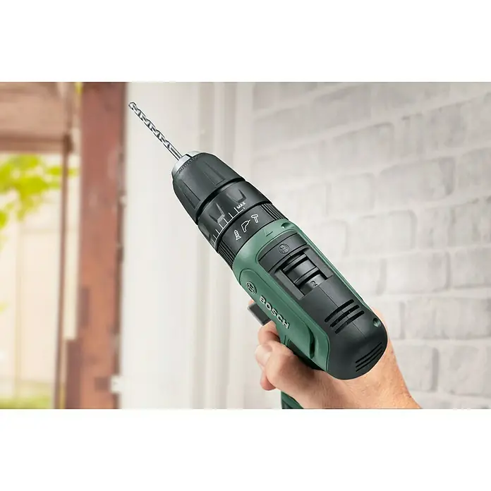 Bosch Taladro atornillador percutor de batería EasyImpact 1200 - 12 V, 1 batería, 1,5 Ah, 30 Nm - Primer plano de un taladro inalámbrico Bosch con broca, sujetado por una mano contra una pared de ladrillo blanco.