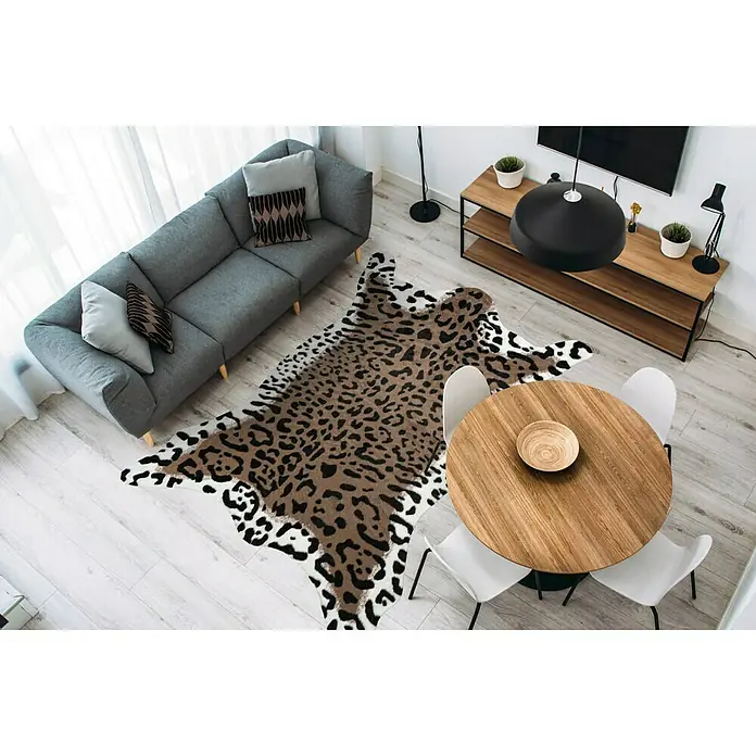 Kayoom Kunstfell Desert - Braun/Weiß, 230 x 160 cm, 85 % Acrylic, 15 % Polyester - Ein stilvoller Wohnraum mit einem grauen Sofa, einem runden Holztisch und einem auffälligen Teppich im Leopardenmuster, der dem Raum einen Hauch von Wildnis verleiht.
