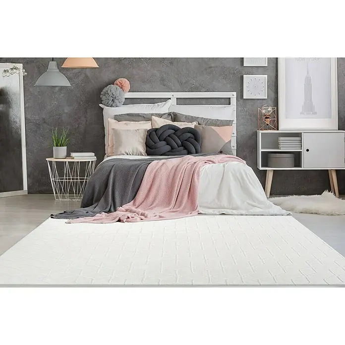 Kayoom Hochflorteppich Vivica 125 - Weiß, 160 x 120 cm - Ein rechteckiger, weißer Teppich mit einem subtilen geometrischen Muster liegt in einem Schlafzimmer mit Bett und Beistelltisch.