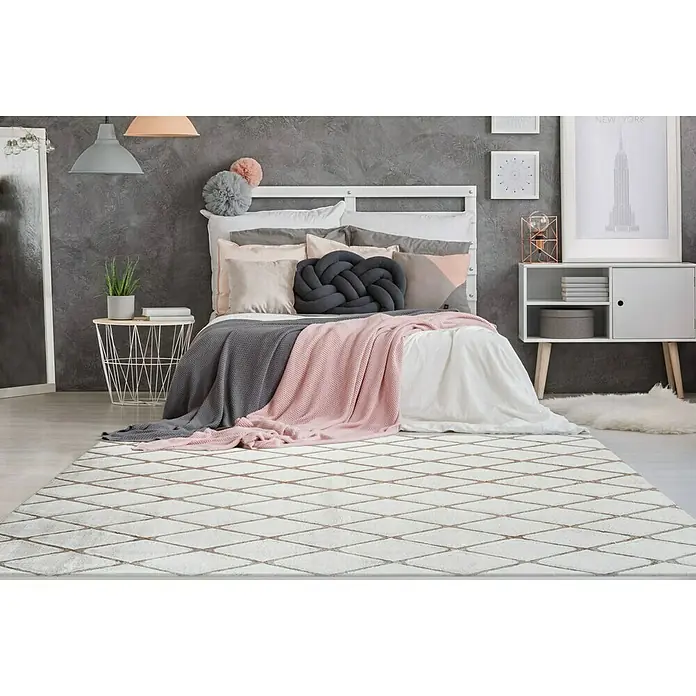 Kayoom Hochflorteppich Vivica 225 - Taupe, 230 x 160 cm - Schlafzimmer mit einem weißen Teppich mit Rautenmuster, Bett, Beistelltisch und Kommode.