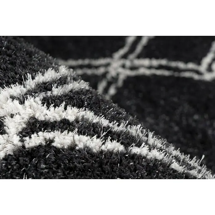 Kayoom Hochflorteppich Orlando 125 - Anthrazit, 230 x 160 cm - Nahaufnahme eines schwarzen Teppichs mit weißem geometrischem Muster, der Textur und Design hervorhebt.