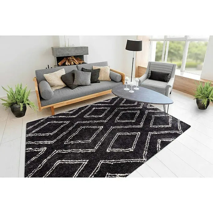 Kayoom Hochflorteppich Orlando 225Anthrazit, 290 x 200 cm, 100 % Polyester - Wohnzimmer mit einem schwarzen Teppich mit geometrischen Mustern, einem grauen Sofa, Sesseln und einem Kaffeetisch.