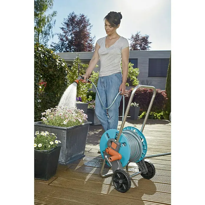 Gardena Kit carro portamangueras Aquaroll S - 20 m - Mujer regando flores con el carro portamangueras Gardena, que se caracteriza por su movilidad y facilidad de uso.