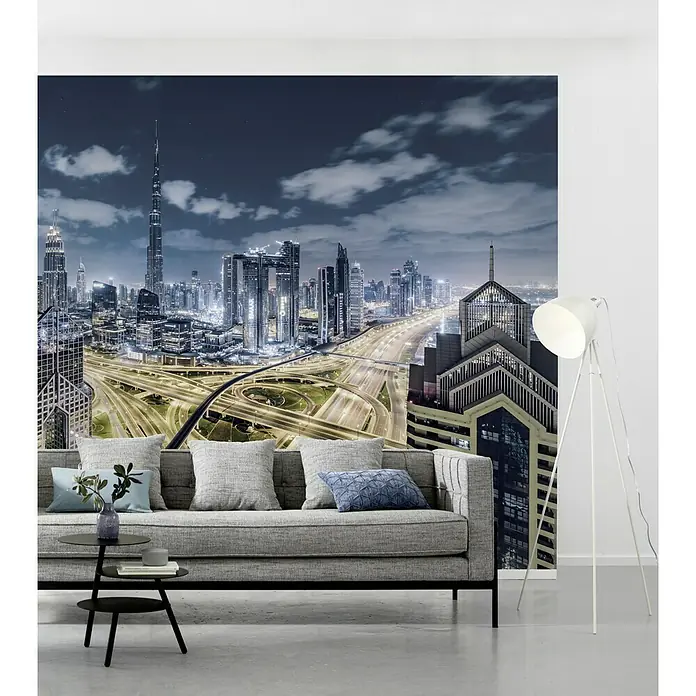 Komar Stefan Hefele Edition 2 Fototapete 1001 Nacht - 9 -tlg., B x H: 450 x 280 cm, Vlies - Elegantes graues Sofa mit Kissen und Beistelltisch vor einer beeindruckenden Skyline-Fototapete, ergänzt durch eine moderne Stehlampe.