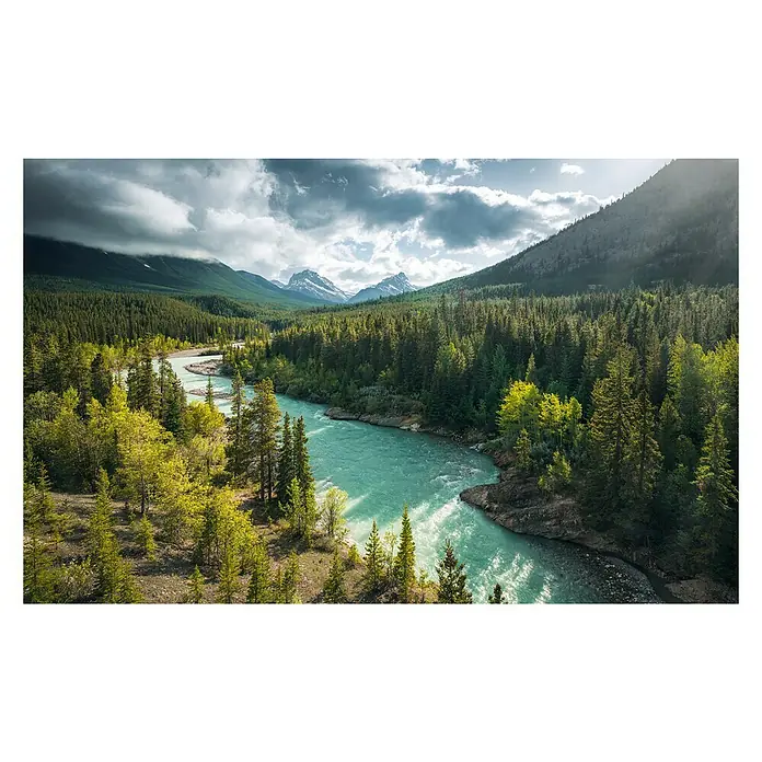 Komar Stefan Hefele Edition 2 Fototapete Wild Canada - 9 -tlg., B x H: 450 x 280 cm, Vlies - Luftaufnahme eines azurblauen Flusses, der sich durch einen grünen Wald schlängelt, mit Bergen und bewölktem Himmel im Hintergrund.