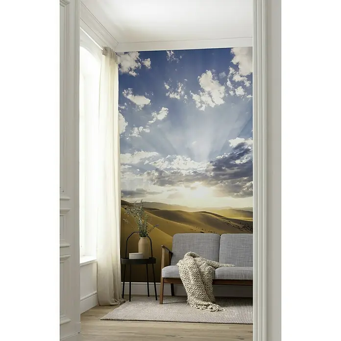 Komar Stefan Hefele Edition 2 Fototapete Wüstenmagie - 4 -tlg., B x H: 200 x 280 cm, Vlies - Wohnzimmer mit Wüstentapete, Sofa und Beistelltisch. Die Tapete zeigt eine sonnige Wüstenlandschaft mit blauem Himmel und Wolken, die dem Raum eine natürliche Note verleiht.