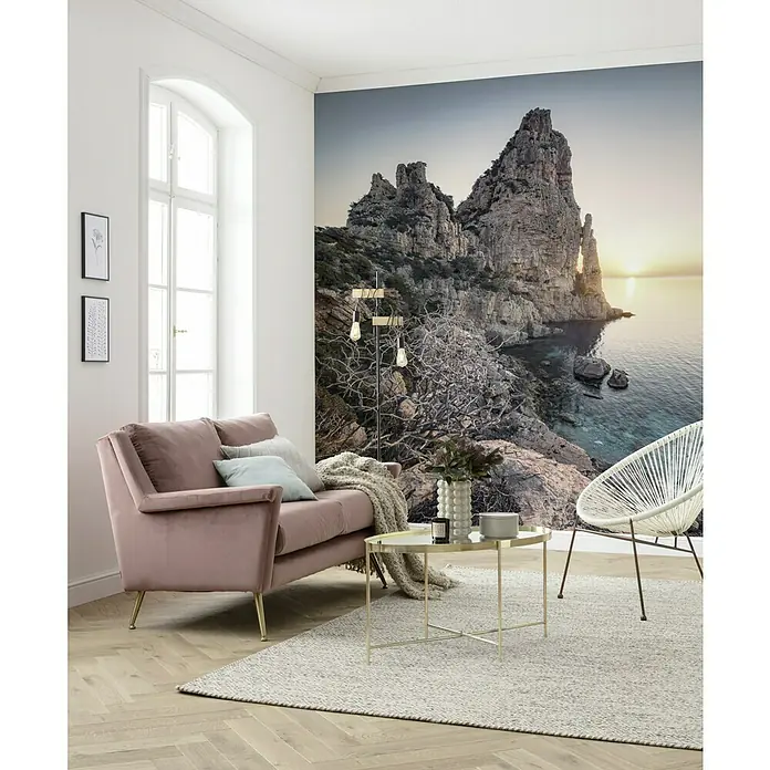 Komar Stefan Hefele Edition 2 Fototapete Colors of Sardegna - 5 -tlg., B x H: 250 x 280 cm, Vlies - Wohnzimmer mit roséfarbenem Sofa, Couchtisch, weißem Sessel und einer Tapete mit Felsformationen, die eine entspannte Atmosphäre schafft.