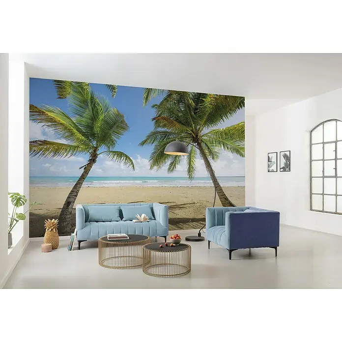 Komar Stefan Hefele Edition 2 Fototapete Carabbean Days II - 9 -tlg., B x H: 450 x 280 cm, Vlies - Einladendes Wohnzimmer mit einer Fototapete, die einen tropischen Strand zeigt, und blauen Polstermöbeln, die eine entspannte Atmosphäre schaffen.