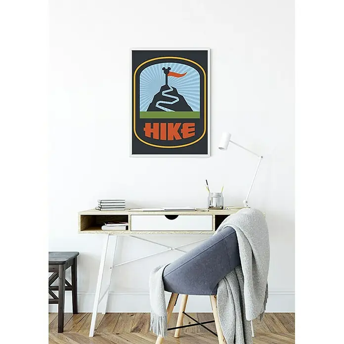 Komar Disney Edition 4 Poster Mickey Mouse Hike - Disney, B x H: 40 x 50 cm - Das Bild zeigt ein dekoratives Wandposter mit einem stilisierten Bergmotiv und der Aufschrift "HIKE", das über einem Schreibtisch hängt.