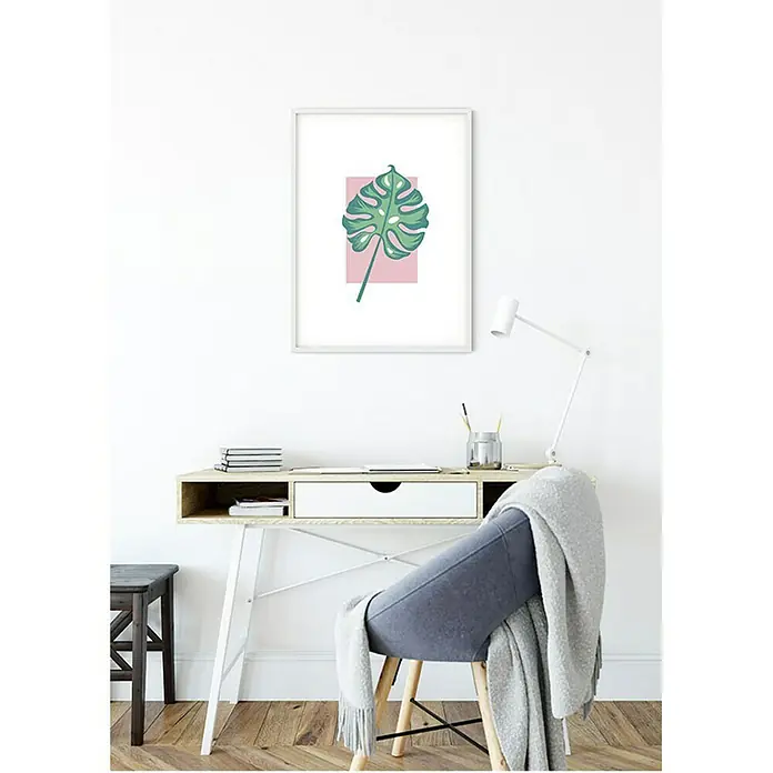 Komar Disney Edition 4 Poster Minnie Mouse Leaf - Disney, B x H: 50 x 70 cm - Das Bild zeigt ein gerahmtes Wandbild mit einem grünen Monstera-Blatt auf rosafarbenem Hintergrund, das über einem Schreibtisch hängt.