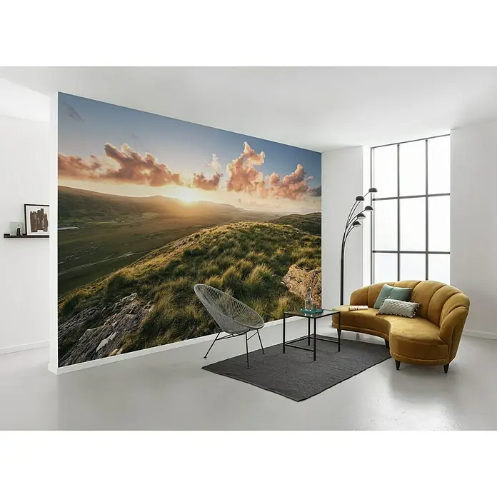 Komar Stefan Hefele Edition 2 Fototapete Abenteuerland - 8 -tlg., B x H: 400 x 280 cm, Vlies - Ein Innenraum mit einer Fototapete, die eine Hügellandschaft bei Sonnenuntergang zeigt, zusammen mit einem Sofa und Möbeln.
