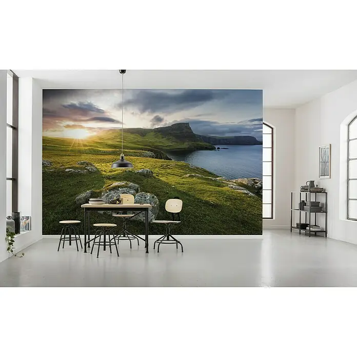 Komar Stefan Hefele Edition 2 Fototapete Scottish Paradise - 9 -tlg., B x H: 450 x 280 cm, Vlies - Ein Esszimmer mit einem Wandbild einer grünen Küstenlandschaft bei Sonnenaufgang, das eine ruhige und einladende Atmosphäre schafft.