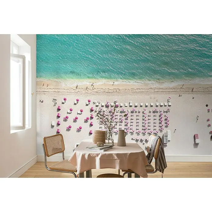 Komar Pure Fototapete Pink Umbrella - 4 -tlg., B x H: 400 x 250 cm, Vlies - Wohnraum mit einem Wandbild von einem Strand, mit türkisfarbenem Wasser und rosafarbenen Sonnenschirmen, das eine entspannte Atmosphäre schafft.