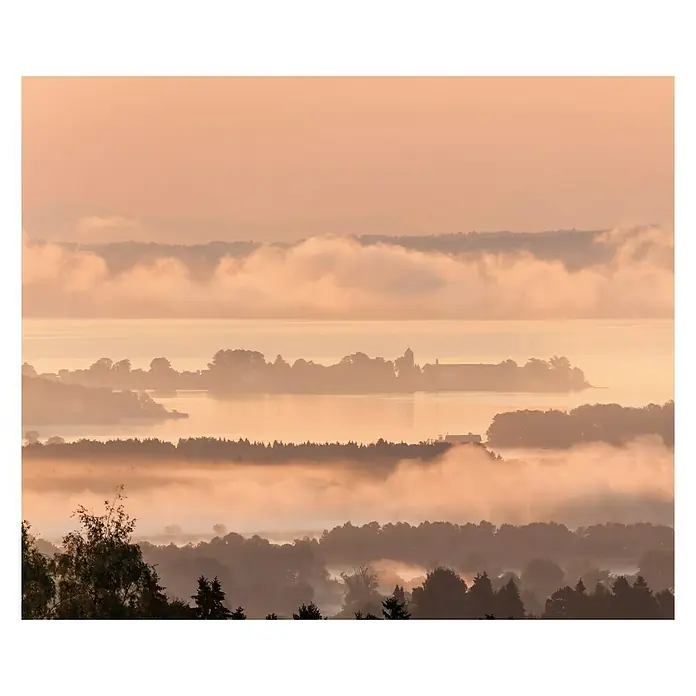 Komar Pure Fototapete Chiemsee - 3 -tlg., B x H: 300 x 250 cm, Vlies - Dramatischer Sonnenaufgang über einer nebelverhangenen Landschaft mit See und Bäumen, eingefangen in warmen, goldenen Farbtönen.