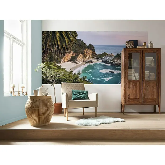 Komar Stefan Hefele Edition 1 Fototapete Paradise Falls - 1 -tlg., B x H: 200 x 100 cm, Vlies - Das helle, moderne Interieur zeigt einen beigen Sessel mit grünen Kissen, einen Beistelltisch aus Rattan und einen hölzernen Bücherschrank.