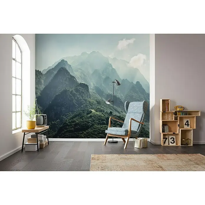 Komar Stefan Hefele Edition 1 Fototapete The Summit - 3 -tlg., B x H: 300 x 200 cm, Vlies - Ein stilvoller Raum mit einem Sessel, einem Tisch, Regalen und einer Bergtapete, die eine ruhige und einladende Atmosphäre schafft.