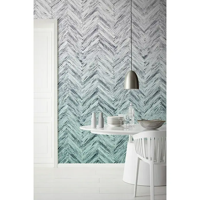 Komar Infinity Fototapete Herringbone Mint4 -tlg., B x H: 400 x 250 cm, Vlies - Weißer Esstisch mit Geschirr und Dekoration vor einer Wand mit blau-grauem Fischgrätmuster, beleuchtet von einer modernen Hängelampe.