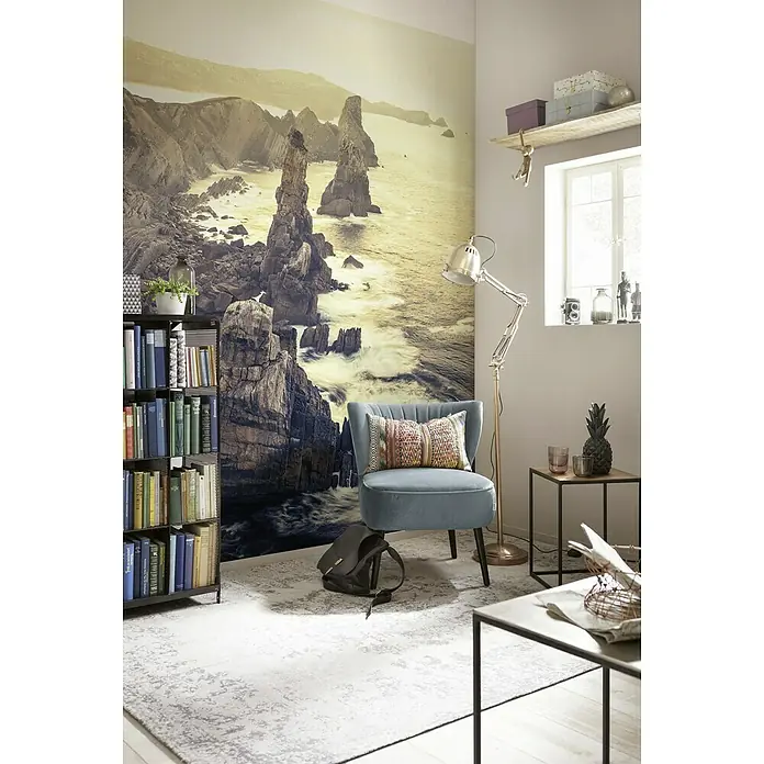 Komar Stefan Hefele Edition 1 Fototapete Pillar Parade - 2 -tlg., B x H: 200 x 250 cm, Vlies - Wohnzimmer mit einem blauen Sessel, Bücherregal und einem Wandbild einer felsigen Küste, das eine ruhige Atmosphäre schafft.