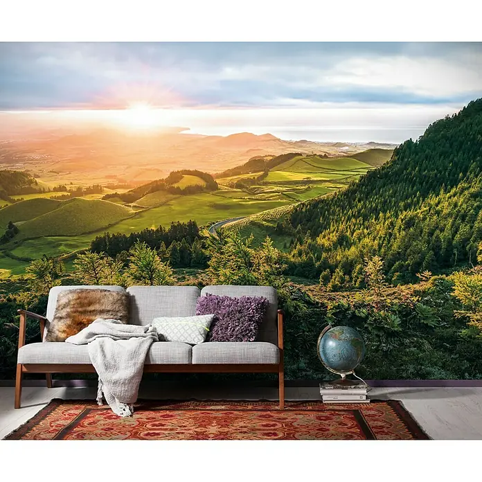 Komar Stefan Hefele Edition 1 Fototapete Paradise Island - 4 -tlg., B x H: 400 x 250 cm, Vlies - Ein stilvolles graues Sofa mit Kissen und Decke vor einer Fototapete mit Landschaftsmotiv, das eine warme und einladende Atmosphäre schafft.