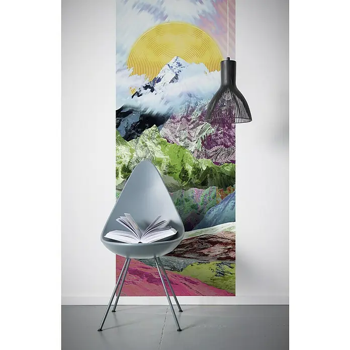 Komar Infinity Fototapete Mountain Top Panel - 1 -tlg., B x H: 100 x 250 cm, Vlies - Das Bild zeigt eine blaue Schalenstuhl mit Buch, eine Hängelampe und eine bunte Bergtapete, die dem Raum eine kreative und entspannende Atmosphäre verleiht.