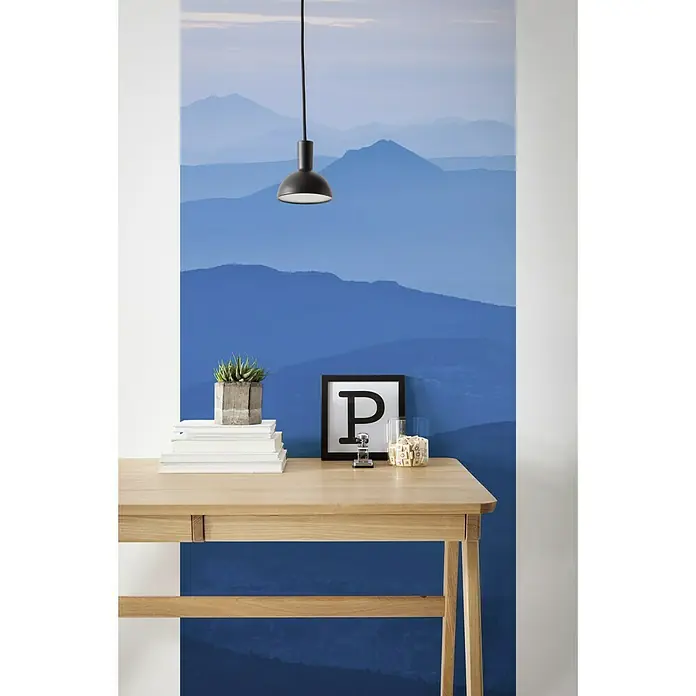 Komar Infinity Fototapete Blue Mountain Panel - 1 -tlg., B x H: 100 x 250 cm, Vlies - Ein hellbrauner Schreibtisch aus Holz mit einer Pflanze, einem Stapel Büchern, einem Briefhalter, einem Rahmen und einem Glas.