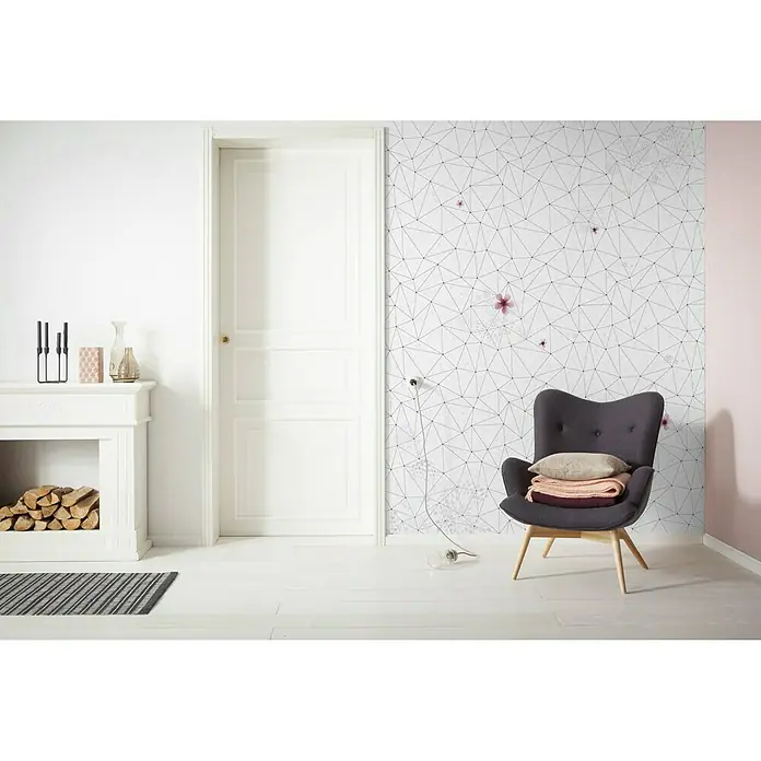 Komar Infinity Fototapete Cherry Blossom - 2 -tlg., B x H: 200 x 250 cm, Vlies - Einrichtungsszene mit einem stilvollen, grauen Sessel mit Kissen und Decke vor einer Wand mit geometrischem Muster. Dekorative Elemente ergänzen das Gesamtbild.