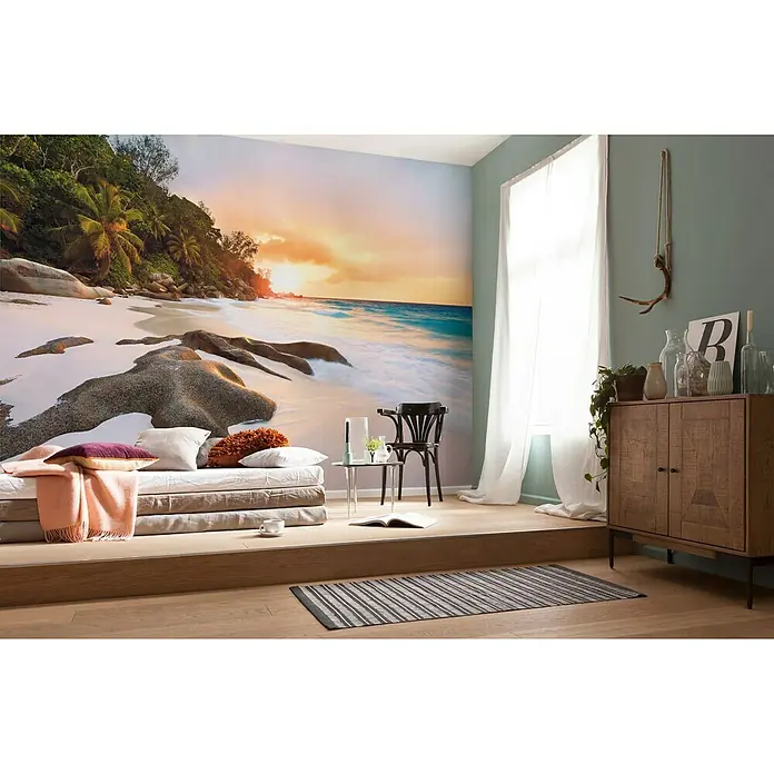 Komar Stefan Hefele Edition 1 Fototapete Nature - 4 -tlg., B x H: 400 x 250 cm, Vlies - Einladender Wohnraum mit einer Fototapete, die einen tropischen Strand bei Sonnenuntergang zeigt. Der Raum ist mit einer gemütlichen Matratze und Holzmöbeln ausgestattet.