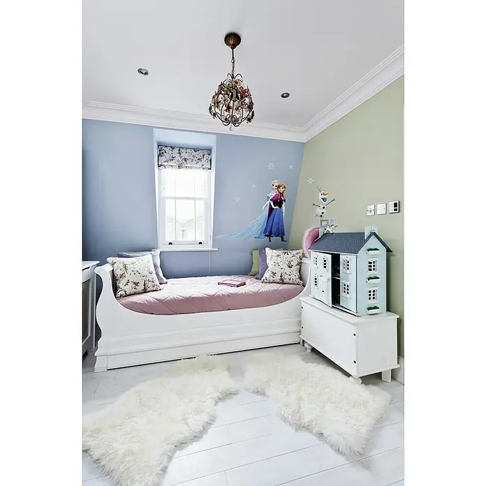 Komar Disney Edition 4 Dekosticker Frozen Sisters - 8 -tlg., Bunt - Einladendes Kinderzimmer mit weißem Bett, pastellfarbenen Wänden und verspielter "Die Eiskönigin"-Dekoration, akzentuiert durch einen dekorativen Kronleuchter.
