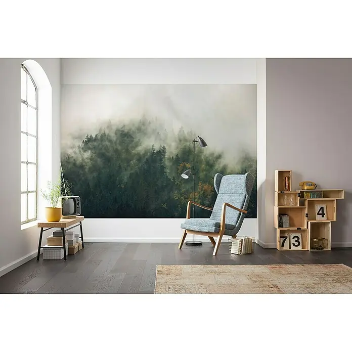 Komar Stefan Hefele Edition 1 Fototapete Tales of the Carpathians - 3 -tlg., B x H: 300 x 200 cm, Vlies - Einrichtungsidee mit einem bequemen Sessel, einem Regal mit Dekorationsgegenständen und einem Wandbild mit Waldmotiv für ein gemütliches Ambiente.