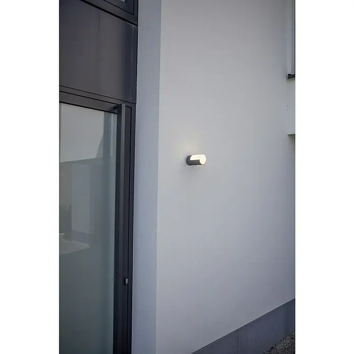 Lutec Plafón LED redondo Cyra - Blanco cálido, IP54 - Una lámpara de pared minimalista ilumina una fachada blanca junto a una puerta moderna.