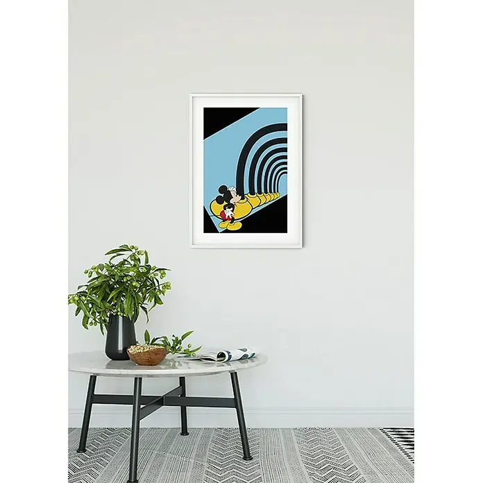 Komar Disney Edition 4 Poster Mickey Mouse Foot Tunnel - Disney, B x H: 50 x 70 cm - Ein gerahmtes Mickey Mouse-Poster hängt an einer Wand über einem Tisch, der mit Dekorationsgegenständen geschmückt ist. Es ist ein stilvolles Kunstwerk.
