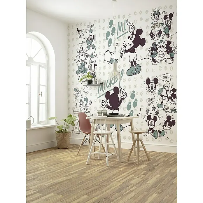 Komar Disney Edition 4 Fototapete Mickey & Friends - 7 -tlg., B x H: 350 x 280 cm, Vlies - Ein Esszimmer mit Holzboden, weißen Wänden und einer Wand mit Mickey Mouse-Motiven, ergänzt durch einen runden Esstisch mit Stühlen.