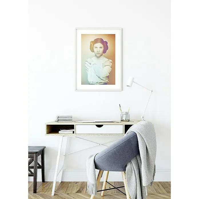 Komar Star Wars Poster Icons Color Leia - Star Wars, B x H: 40 x 50 cm - Das gerahmte Star Wars Leia Poster hängt über dem minimalistischen Schreibtisch mit Stuhl und Schreibtischlampe in einem hellen Raum.