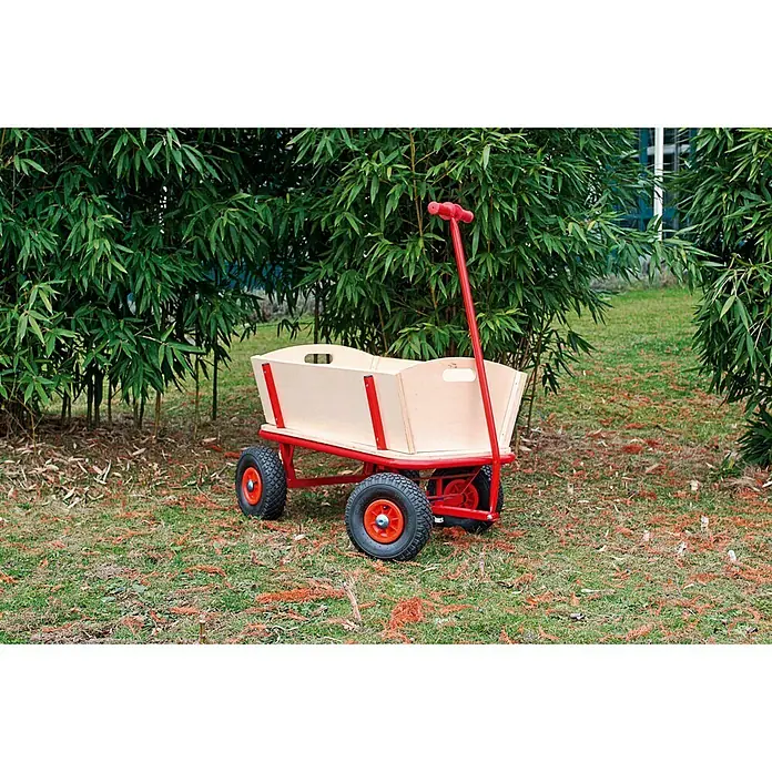 Bollerwagen Bubi - L x B x H: 88 x 60 x 56 cm, Holz - Ein roter Bollerwagen mit einer Holzkiste steht im Garten, umgeben von Grünpflanzen. Ideal für Kinder zum Spielen oder für den Transport leichter Lasten.