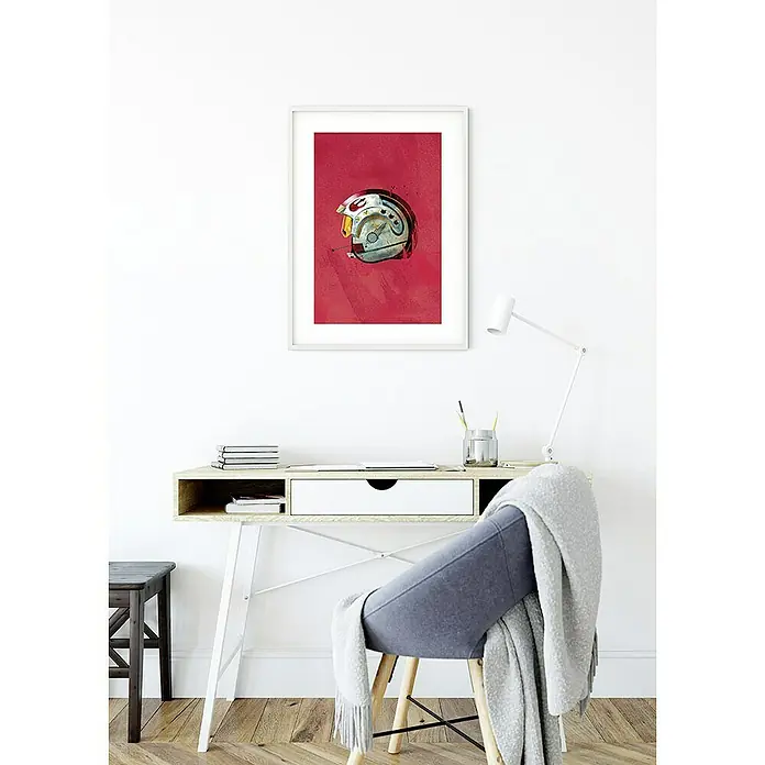 Komar Star Wars Poster Helmets Rebel Pilot - Star Wars, B x H: 40 x 50 cm - Ein gerahmtes Star Wars-Kunstwerk mit dem Design eines Helms hängt an der Wand über einem Schreibtisch mit Stuhl und Lampe.