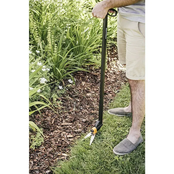Fiskars Rasenkantenschere Servo-System GS46 - Länge: 101,2 cm - Eine Person verwendet eine Fiskars-Rasenkantenschere, um Gras entlang eines Blumenbeets zu schneiden. Die Schere hat einen langen Griff.