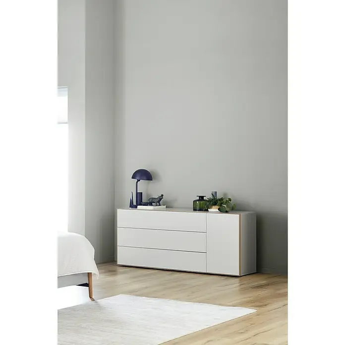 SCHÖNER WOHNEN-Farbe Wandfarbe Trendfarbe - Dreamy, Matt, 5 l, Konservierungsmittelfrei - Eine moderne Kommode in Weiß mit dekorativen Objekten wie einer Lampe und Pflanzen, die ein stilvolles Ambiente schafft.