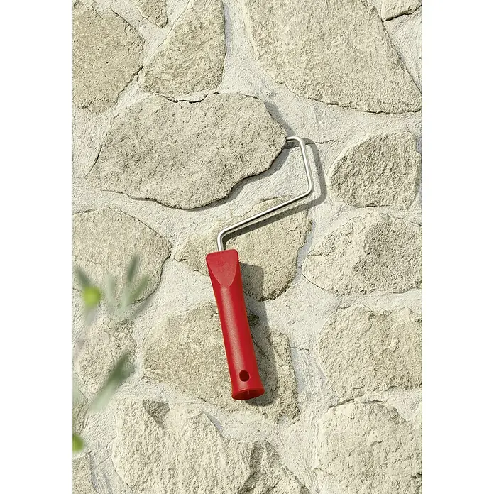 SCHÖNER WOHNEN-Farbe Farbtester Trendfarbe - Finca, Matt, 50 ml, Konservierungsmittelfrei - Nahaufnahme eines roten Farbrollergriffs vor einer hellen Steinwand.