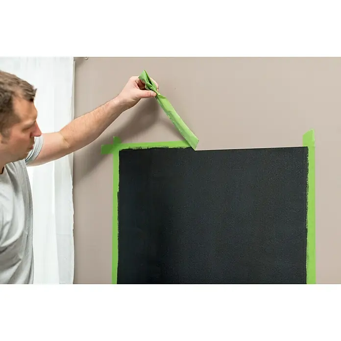 Frogtape Kreativklebeband Multi-Surface - 41,1 m x 36 mm, Grün, 1 -tlg. - Mann entfernt grünes Klebeband von einer frisch gestrichenen schwarzen Tafel an einer Wand, um saubere Kanten zu enthüllen.