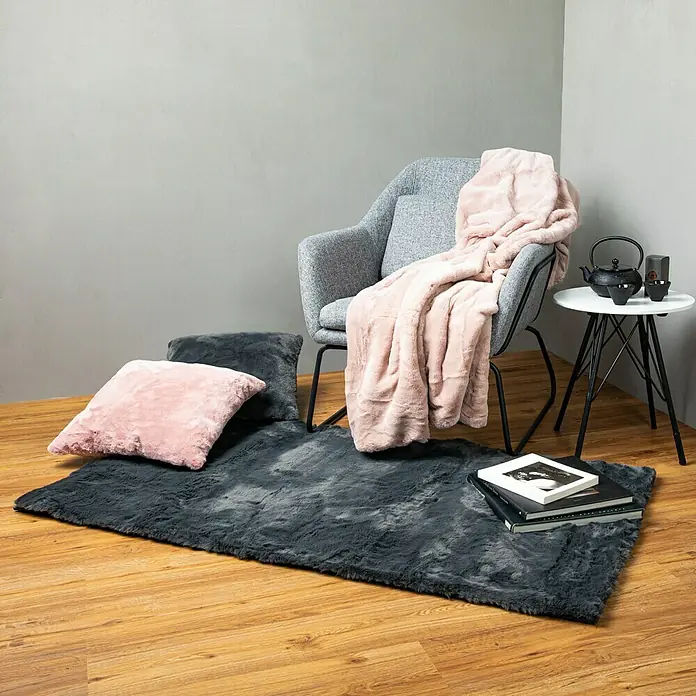 Fellteppich Happy - Graphit, 150 x 80 cm, 100 % Polyester (Flor) - Ein grauer Teppich liegt auf dem Holzboden neben einem Sessel mit rosa Decke. Eine Teekanne und Bücher dekorieren den Raum stilvoll.