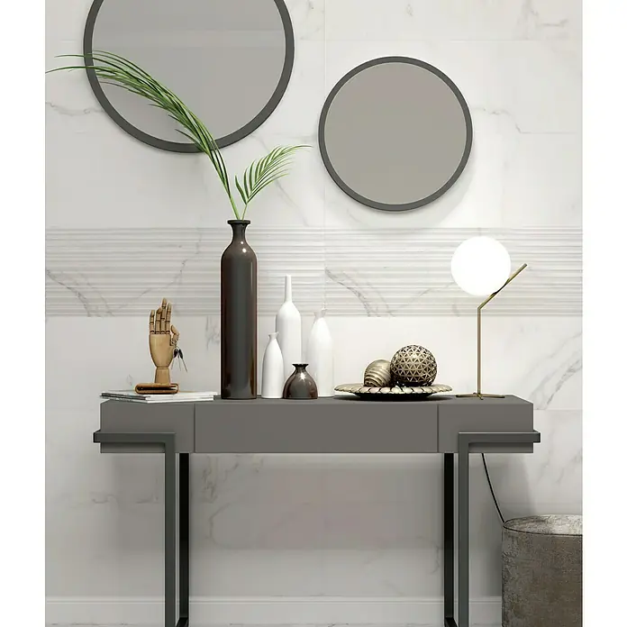 Revestimiento de pared Palatina Nazca - 30 x 90 cm, Blanco Carrara, Mate, Rectificado - Una elegante mesa consola gris con objetos decorativos y espejos contra una pared de mármol blanco, destacando el diseño elegante del producto.