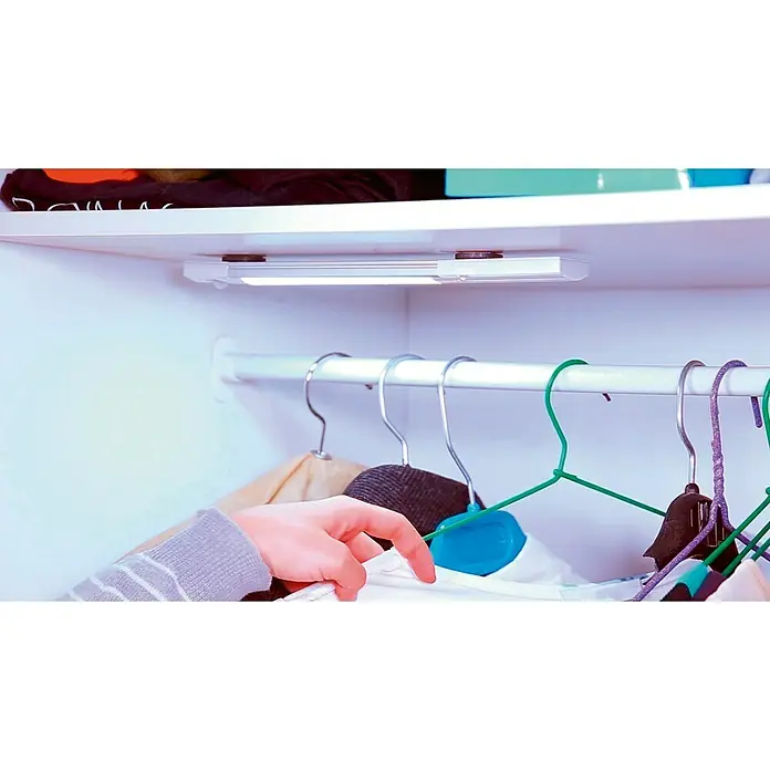 Simon Regleta LED Cresida - 1,3 W, Blanco - Primer plano de una luz LED de armario que ilumina el interior de un armario con ropa colgada, destacando una solución de iluminación brillante y eficiente.