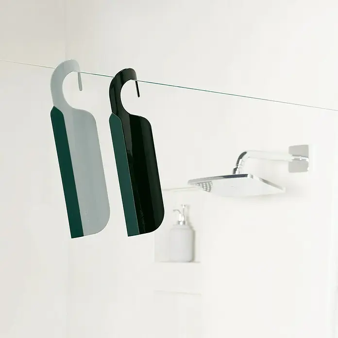 Spirella Bad- & Duschabzieher Skate - Kunststoff, Taupe - Zwei Duschabzieher in Grau und Schwarz hängen an einer Glaswand im Badezimmer, wobei eine Duschbrause und eine Seifenspenderflasche im Hintergrund zu sehen sind.