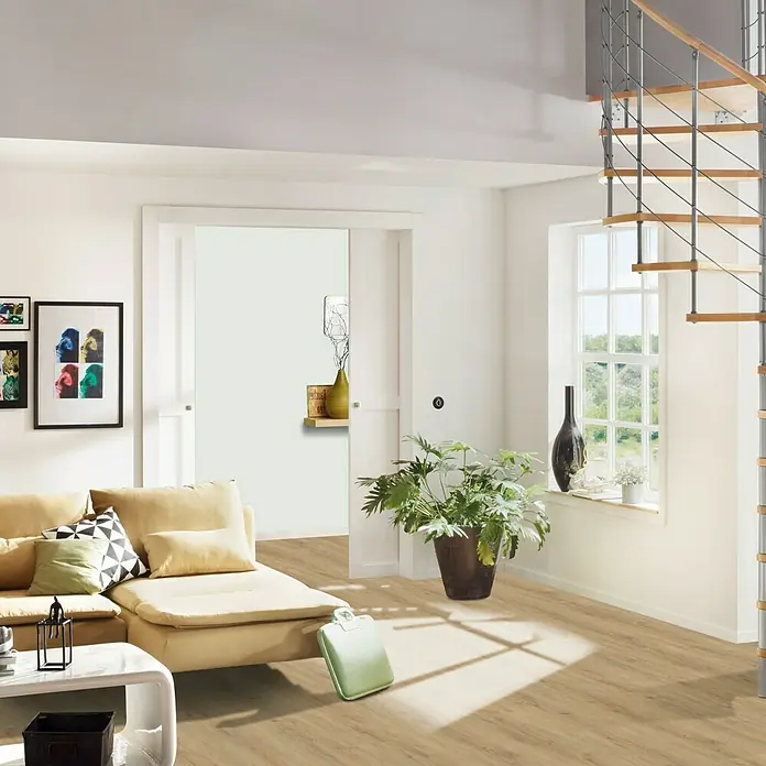 b!design Vinylbodenmuster Rigid Maxi Ashton Eiche - 281 x 161 x 4,8 mm, Landhausdiele - Wohnzimmer mit beiger Couch, Pflanze im Topf und hellen Bodenbelägen für ein modernes und einladendes Ambiente.